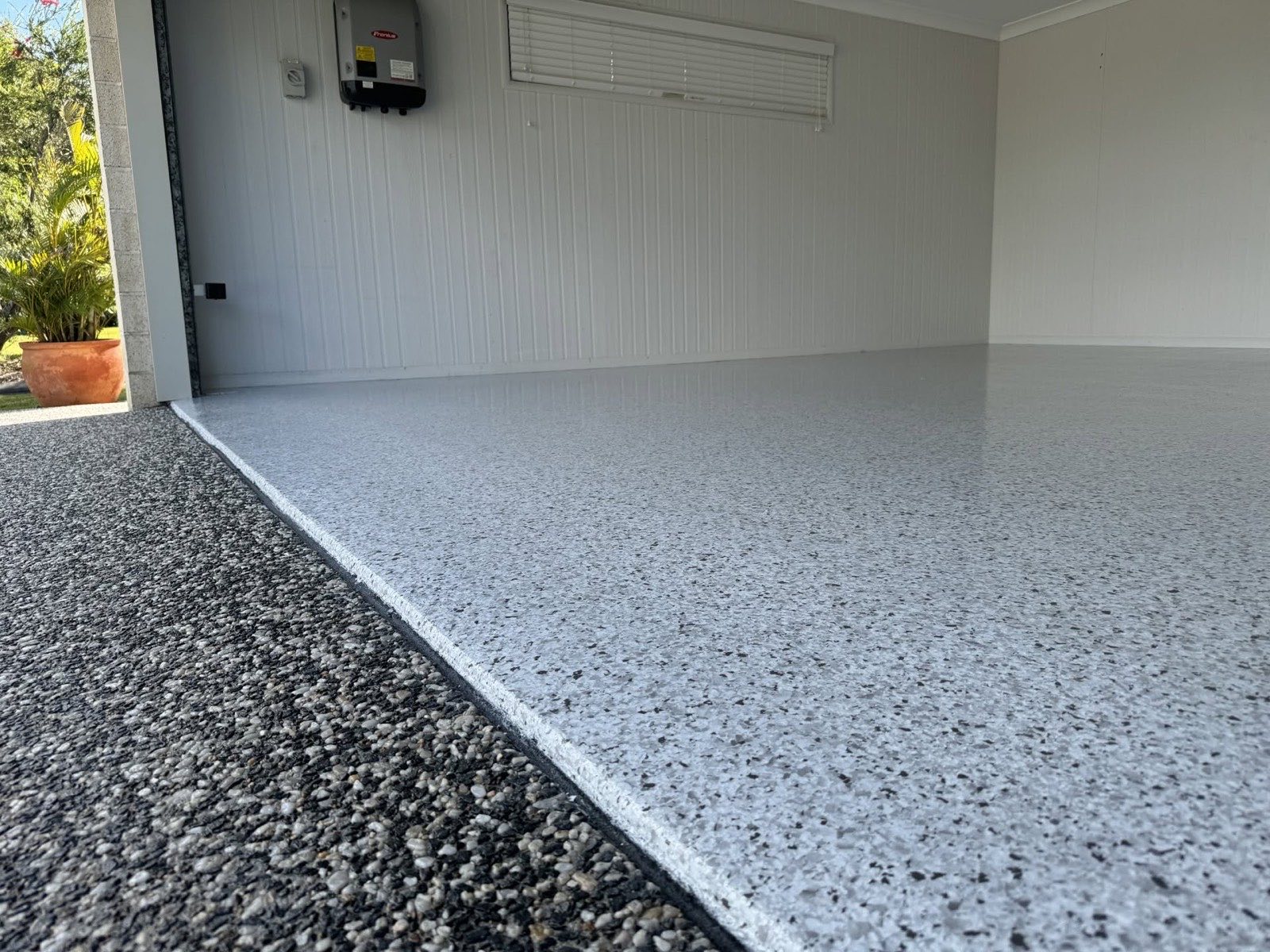 Grey flake epoxy garage floor meeting an exposed aggregate driveway