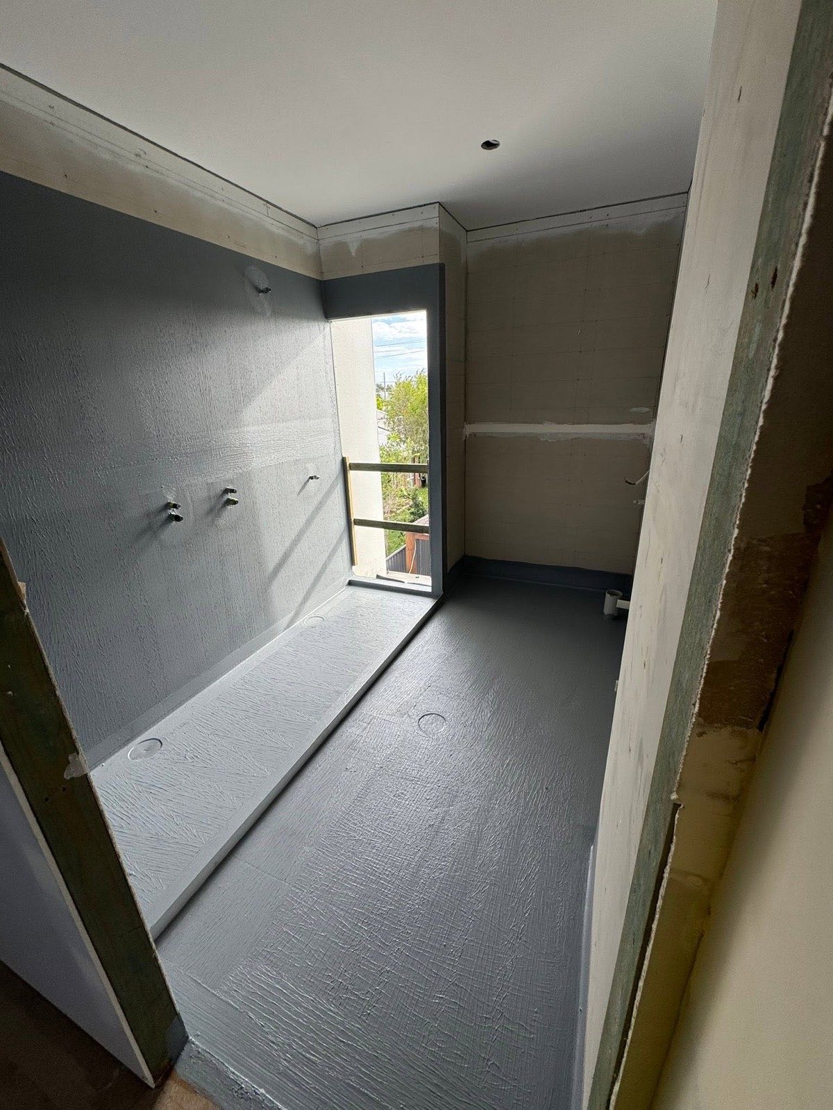 Grey waterproofing membrane applied over a bathroom floor and walls