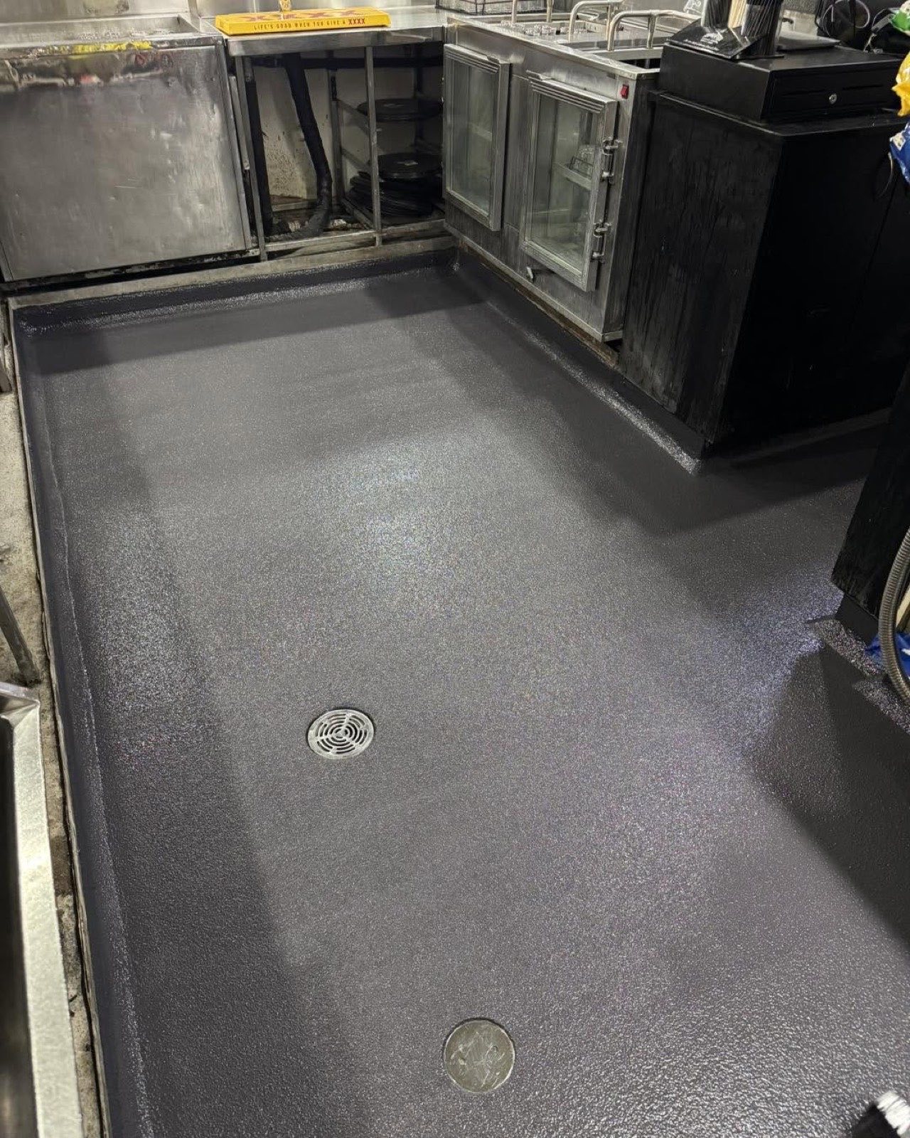 Dark non-slip epoxy floor with coved edges and a drain in a commercial kitchen