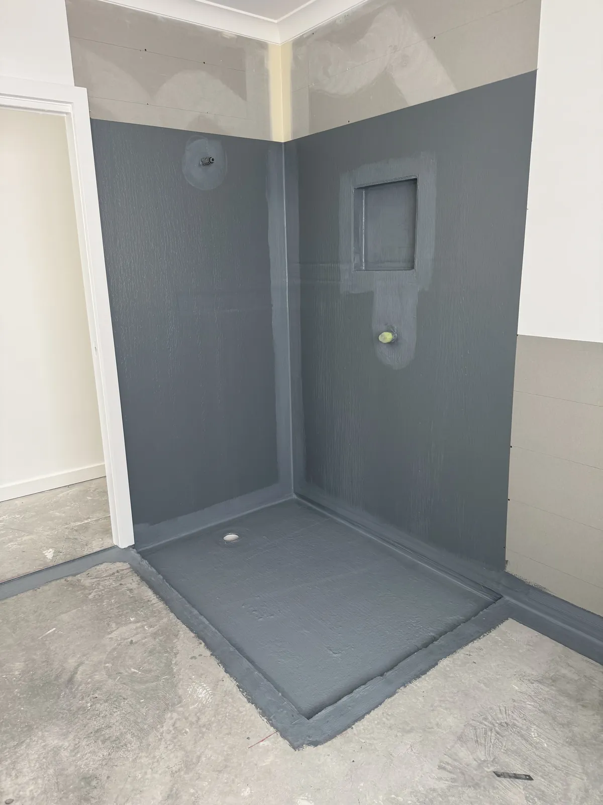 Shower recess fully coated in grey waterproofing membrane, including the wall niche and the shower floor