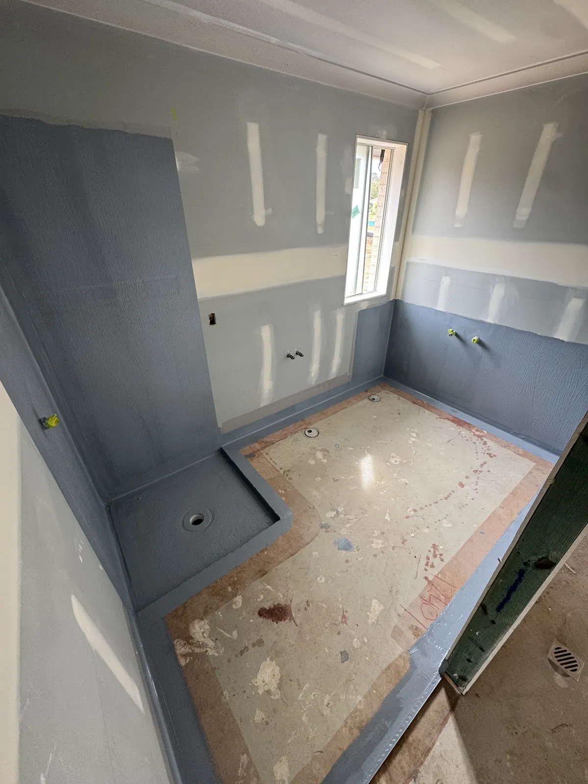 Bathroom with grey waterproofing membrane up the shower walls and around the floor edges, corners treated before tiling