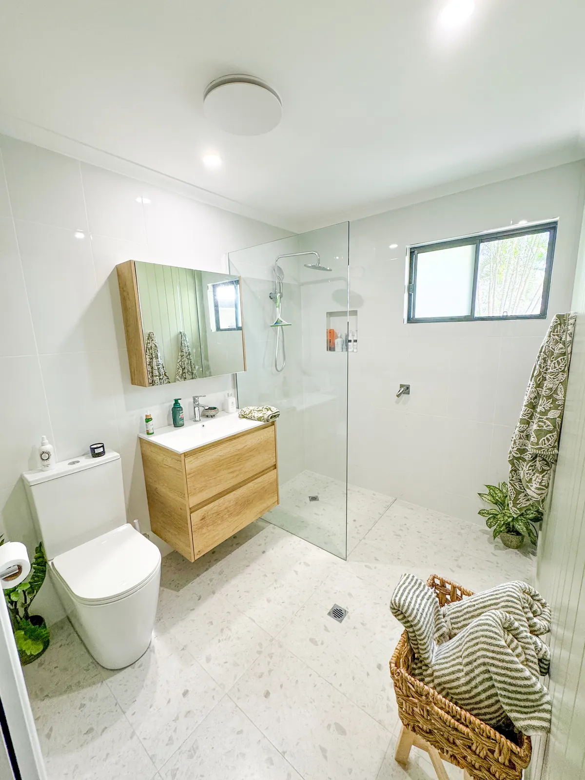 The finished bathroom after waterproofing and tiling, with a frameless glass shower, timber vanity and terrazzo-look floor tiles