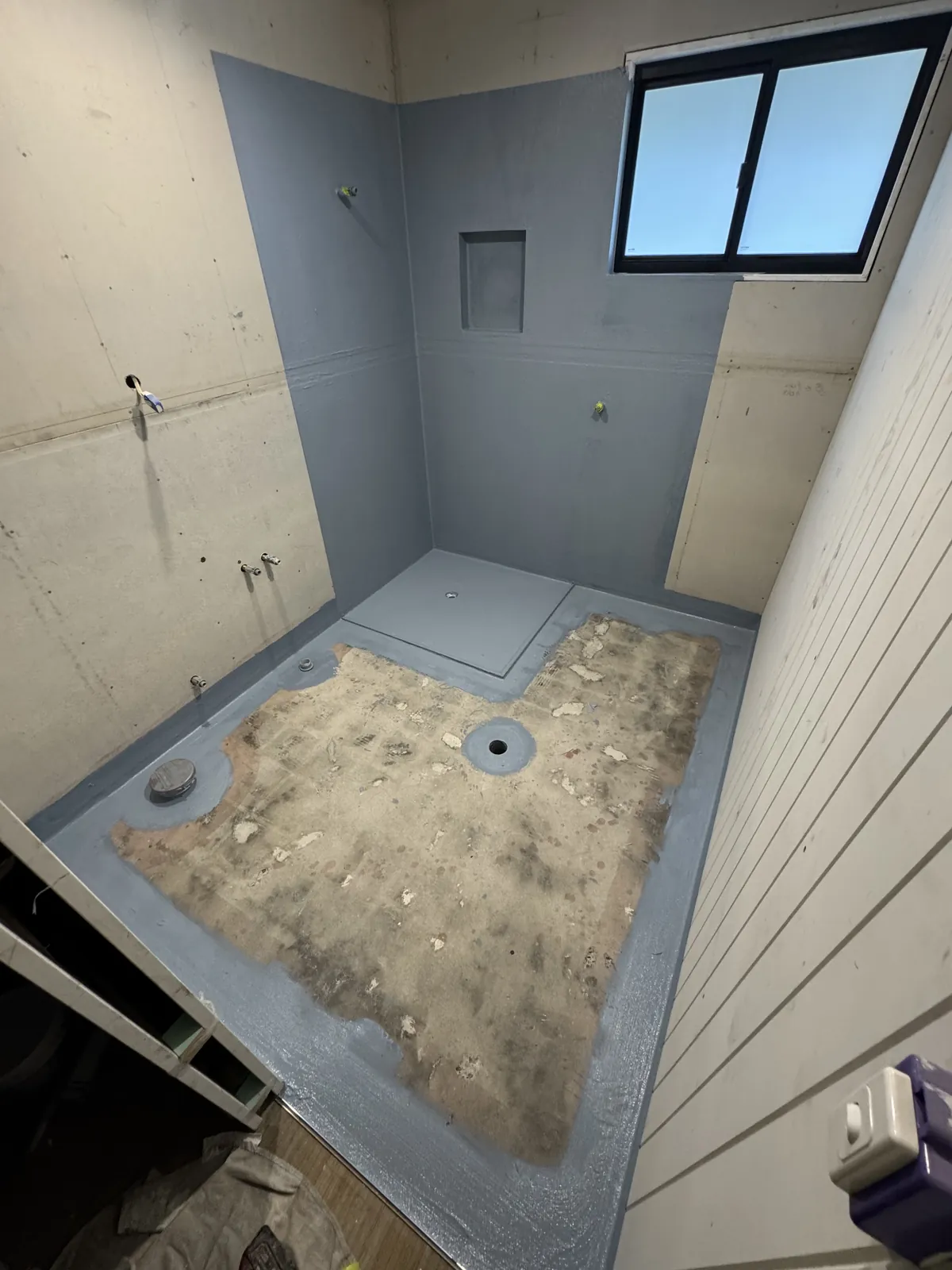 Bathroom mid-waterproofing, with grey membrane on the shower walls and niche and around the floor edges, the main floor still to go