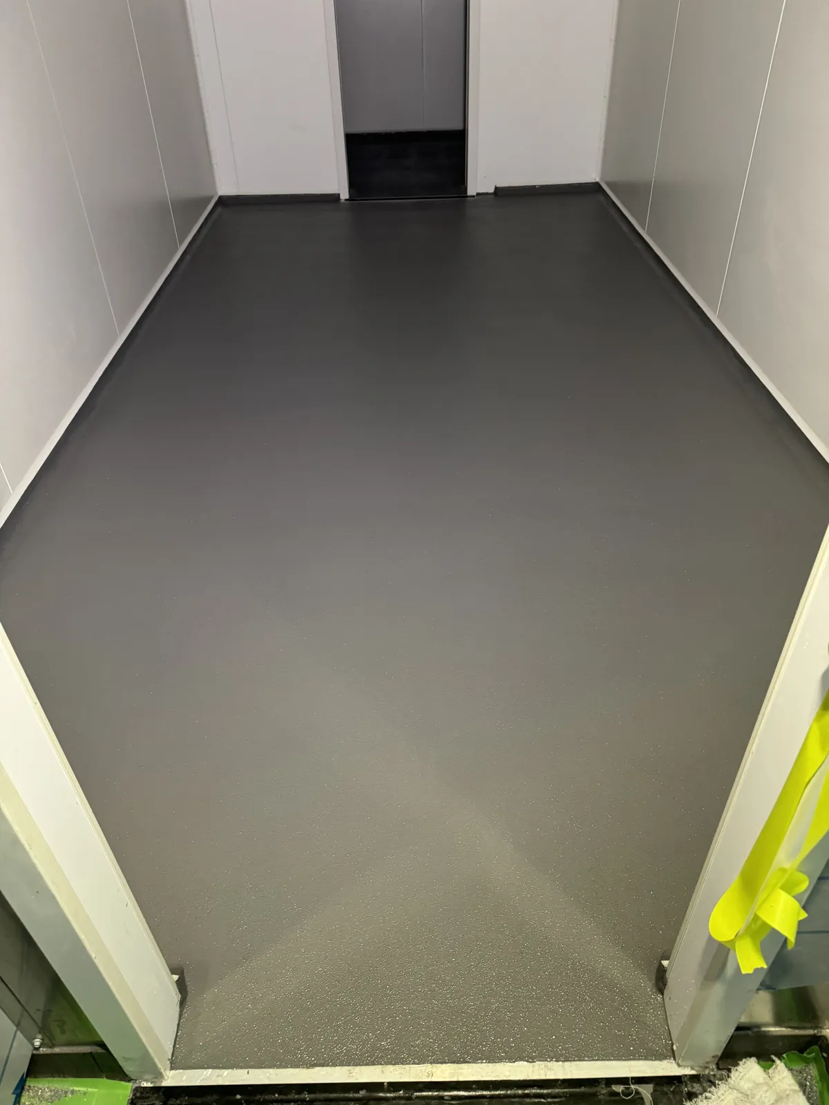 Grey hi-impact epoxy floor coved up the white insulated panel walls of a commercial cold room