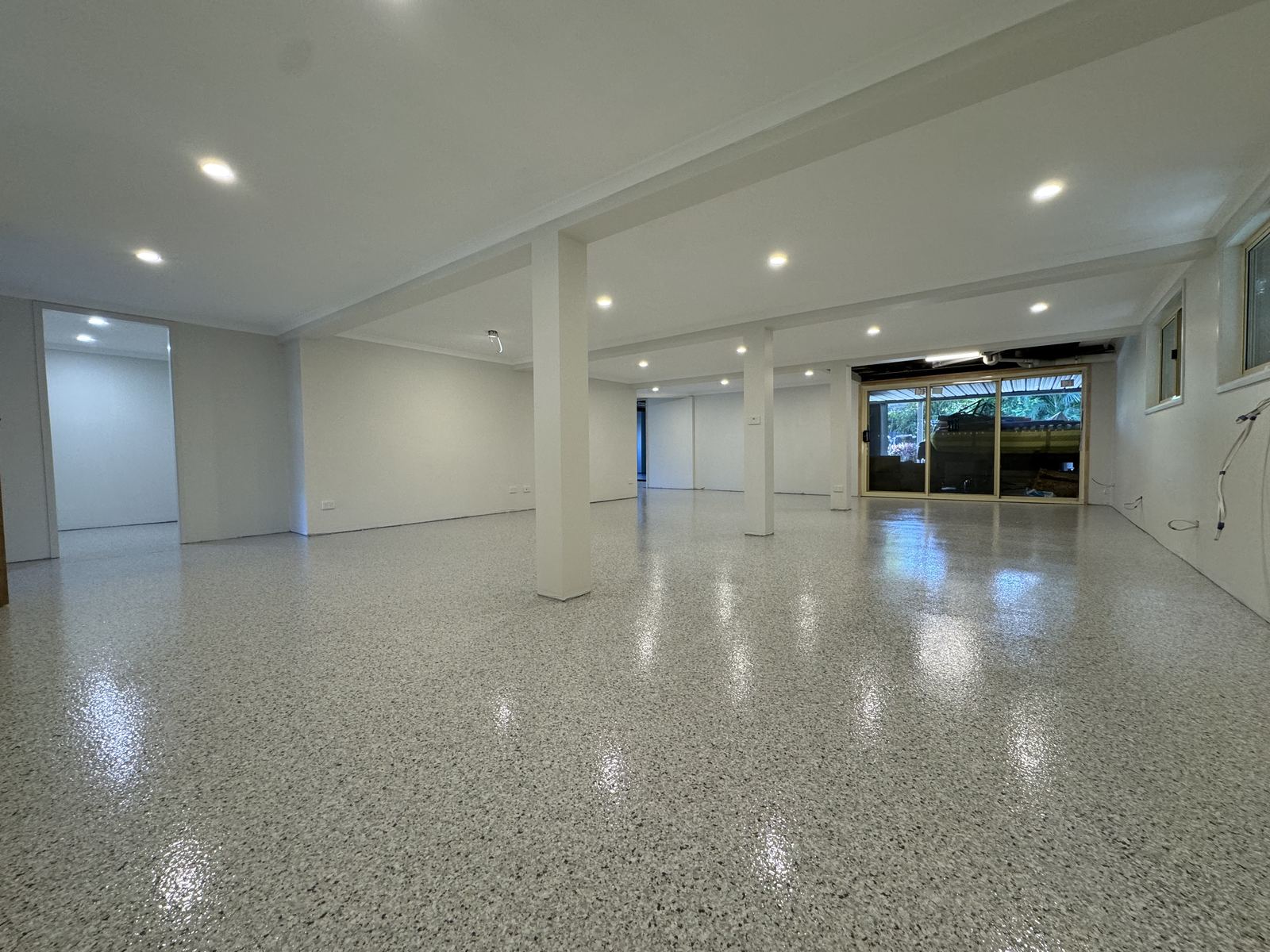 Large open interior space with support columns and downlights, finished in a high-gloss pale flake epoxy floor reflecting the ceiling lights
