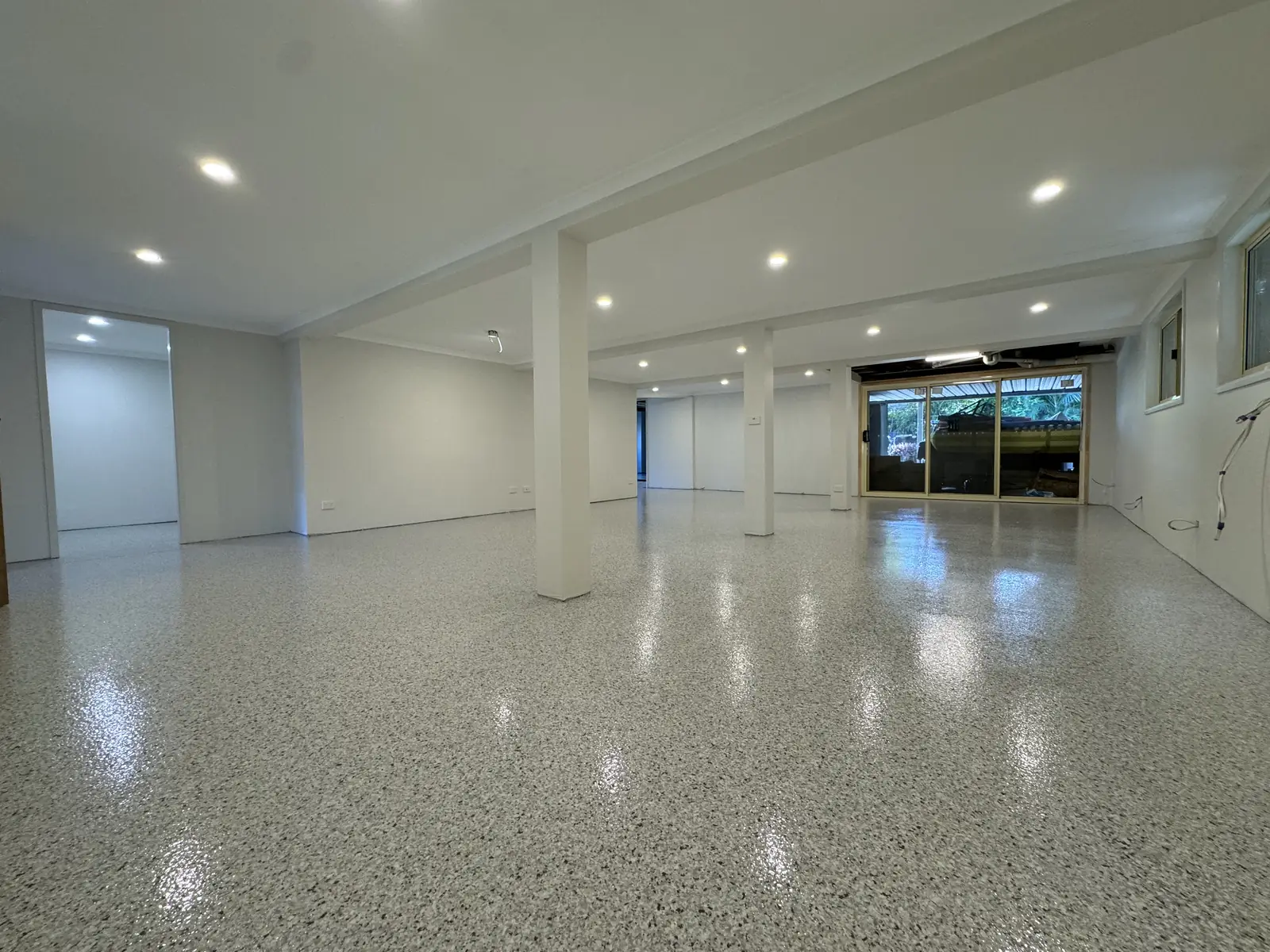Large open interior space with support columns and downlights, finished in a high-gloss pale flake epoxy floor reflecting the ceiling lights