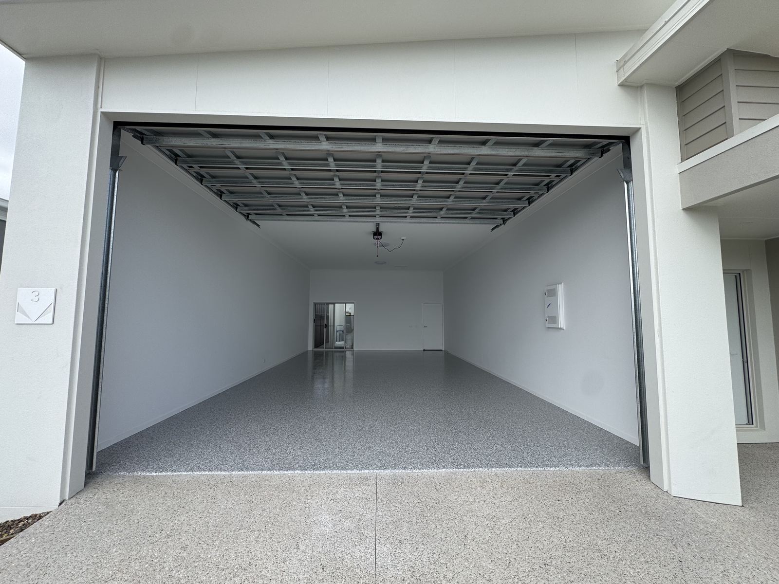 Deep double garage with the roller door up, the light grey flake epoxy floor running the full length to the internal door