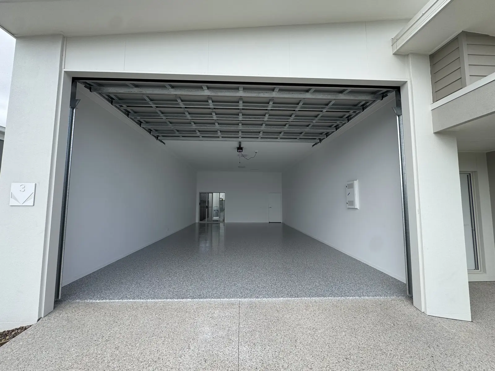 Deep double garage with the roller door up, the light grey flake epoxy floor running the full length to the internal door