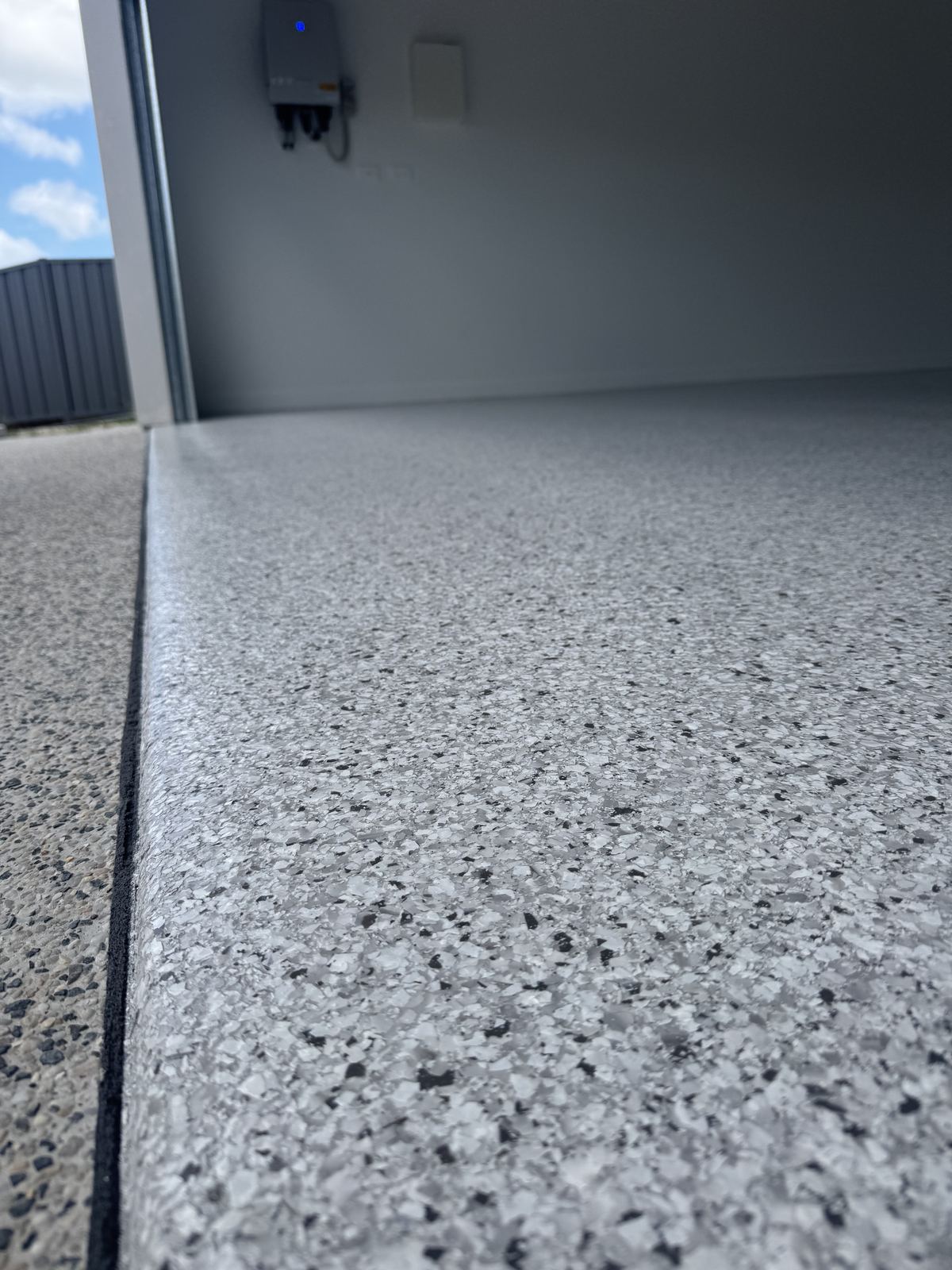 Close view along a grey and black flake epoxy garage floor, showing the crisp sealed edge where the coating meets the door threshold