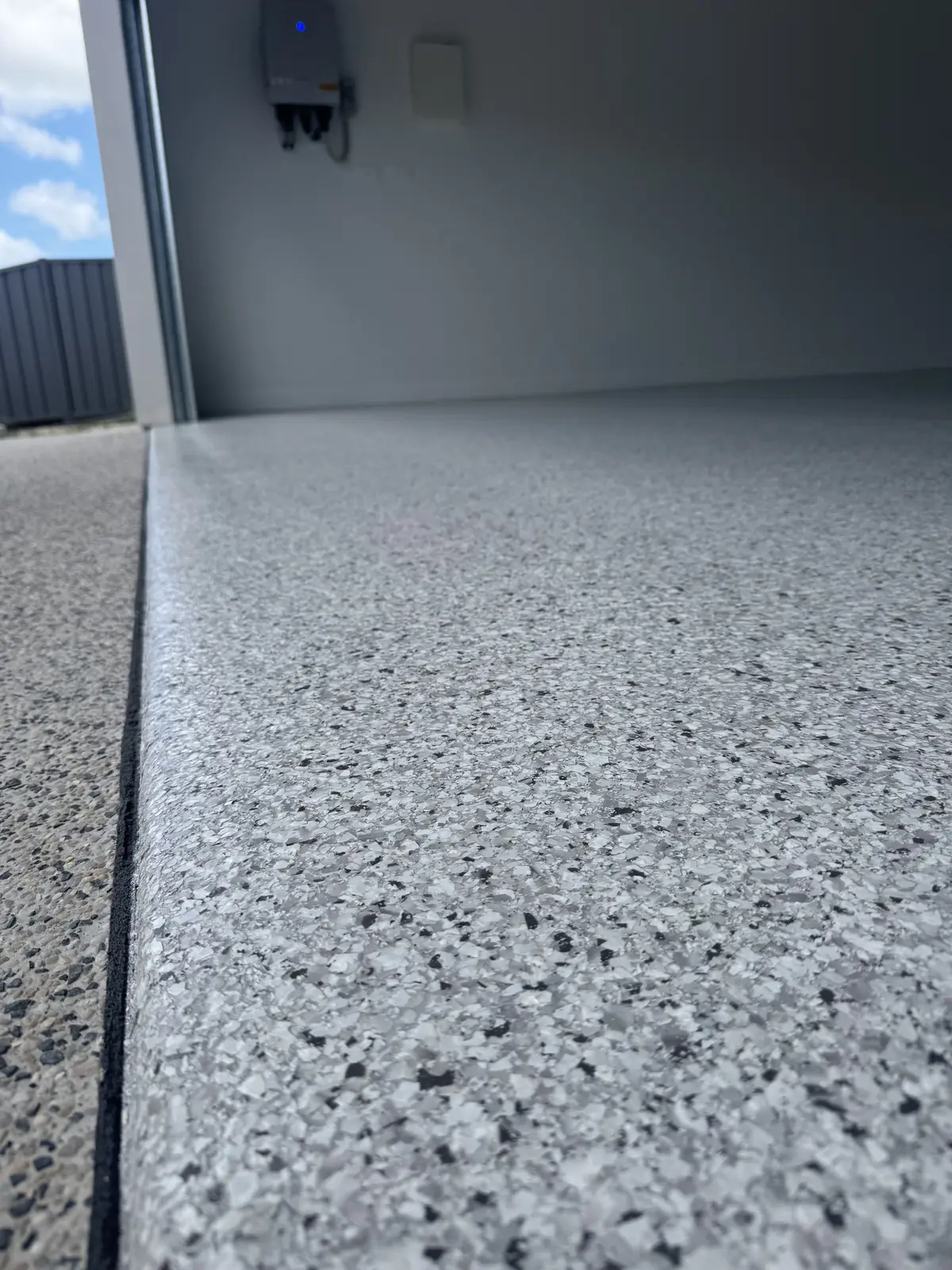 Close view along a grey and black flake epoxy garage floor, showing the crisp sealed edge where the coating meets the door threshold