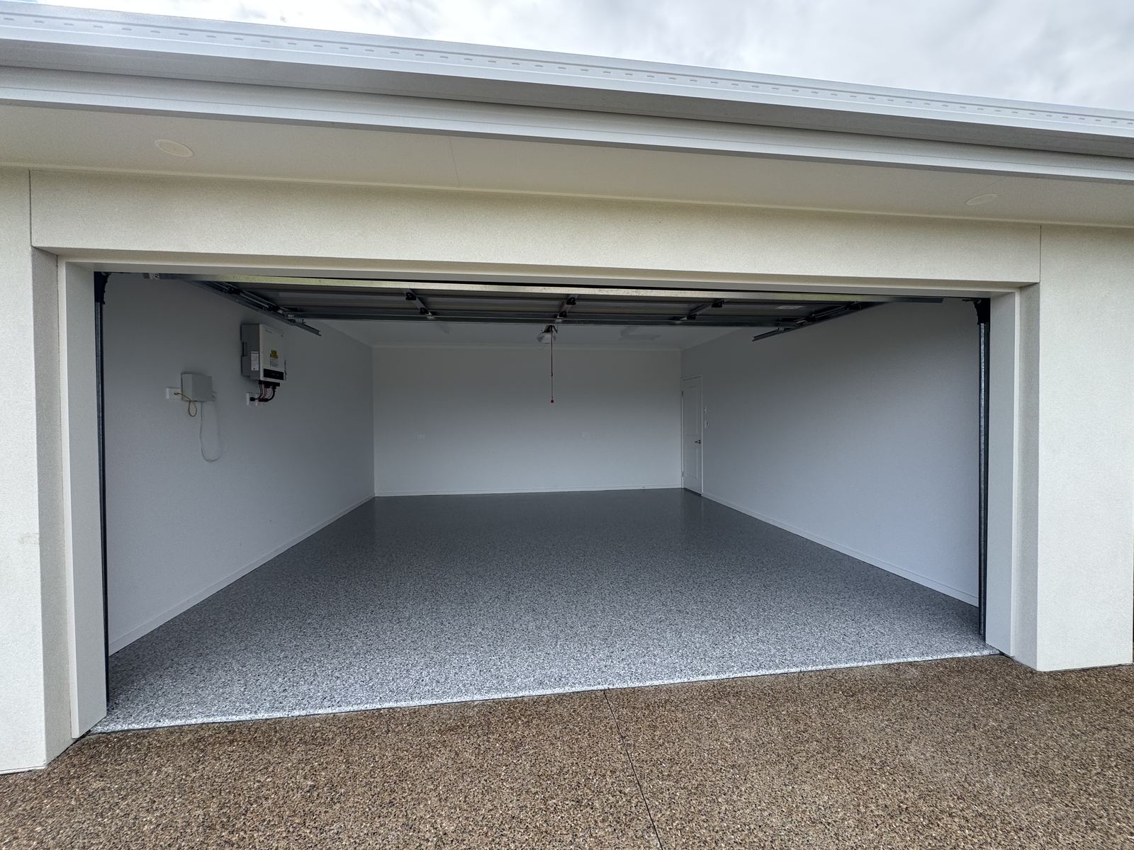 Double garage with the roller door open, showing a grey flake epoxy floor laid wall to wall against white walls