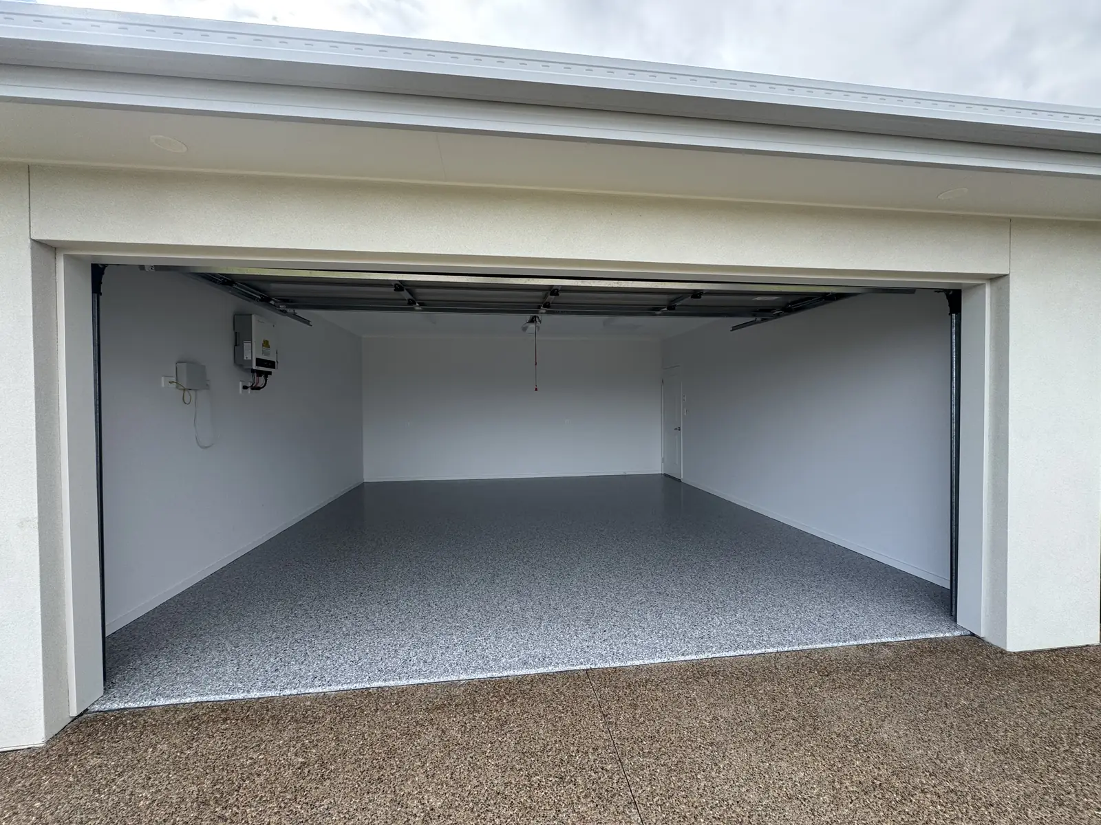 Double garage with the roller door open, showing a grey flake epoxy floor laid wall to wall against white walls