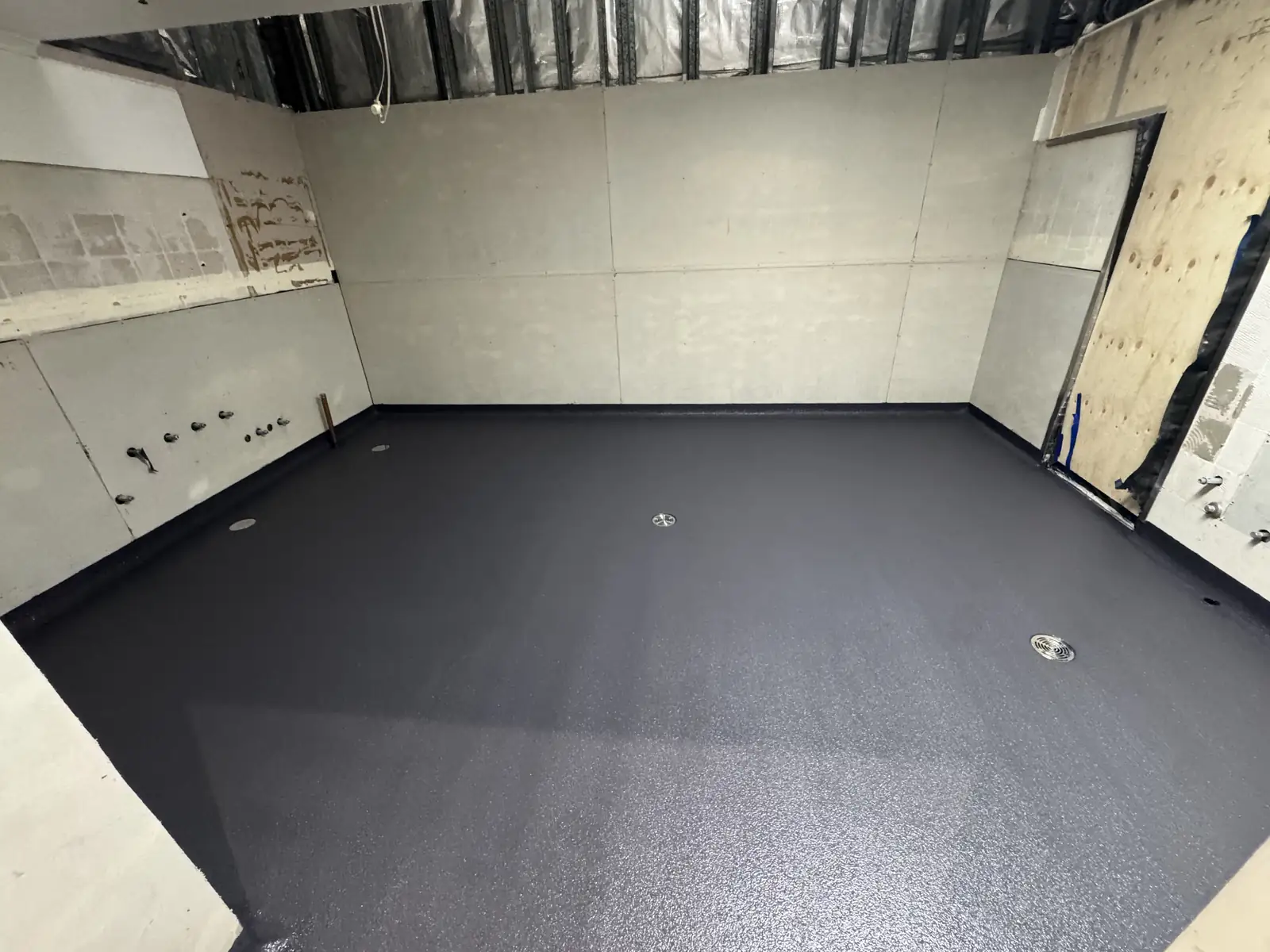 Dark grey hi-impact epoxy floor laid wall to wall in an empty commercial back-of-house room, with two floor wastes