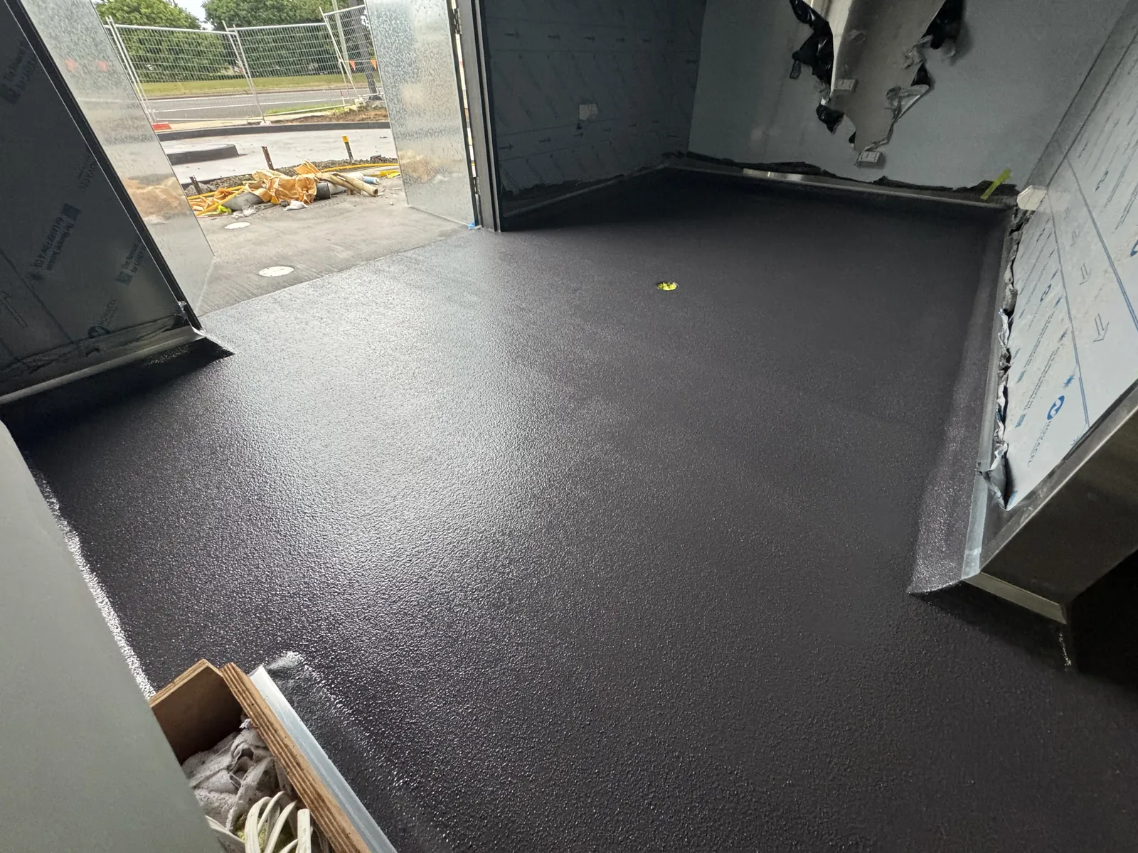 Charcoal hi-impact epoxy floor coved up the walls of a commercial room, with the external door open to a building site