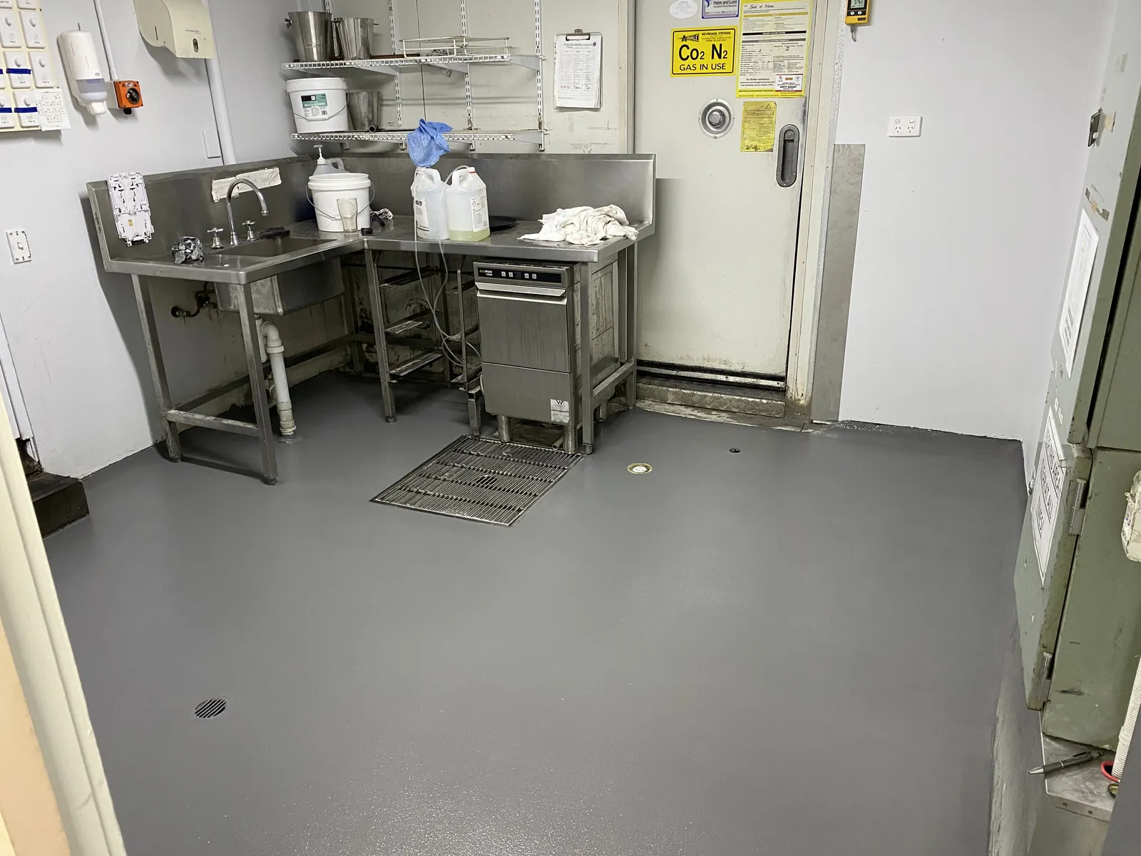 Grey hi-impact epoxy floor in a commercial kitchen, coved up the walls, with floor wastes between the stainless benches