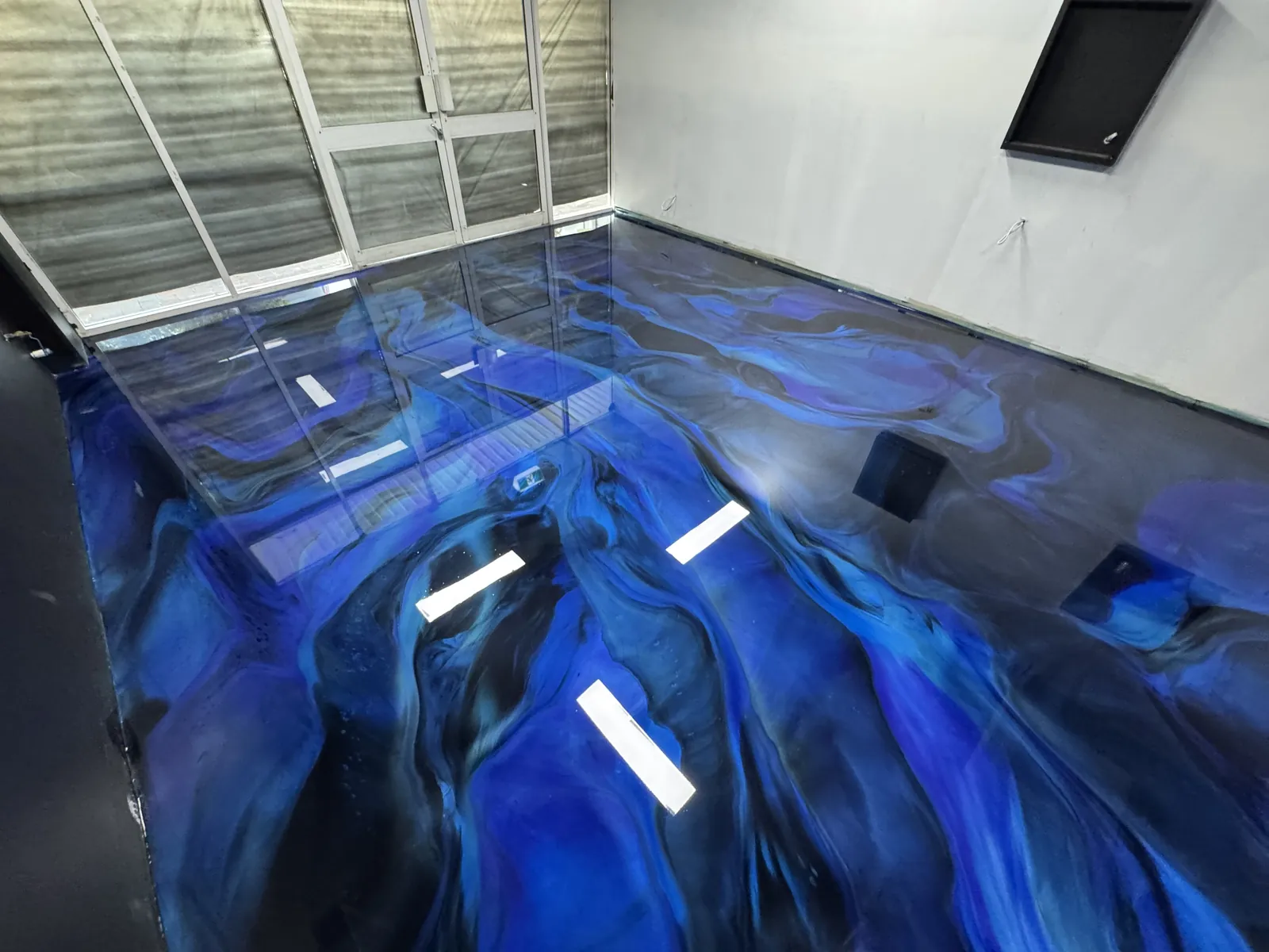 Blue marbled metallic epoxy floor in an empty room, the gloss coat reflecting the lights and windows