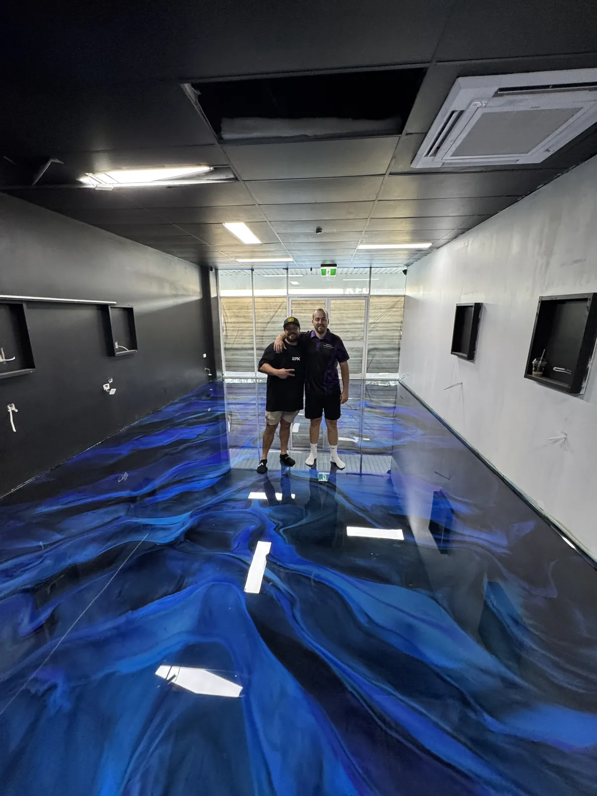 Two men standing at the far end of a finished blue metallic epoxy floor in a commercial fit-out