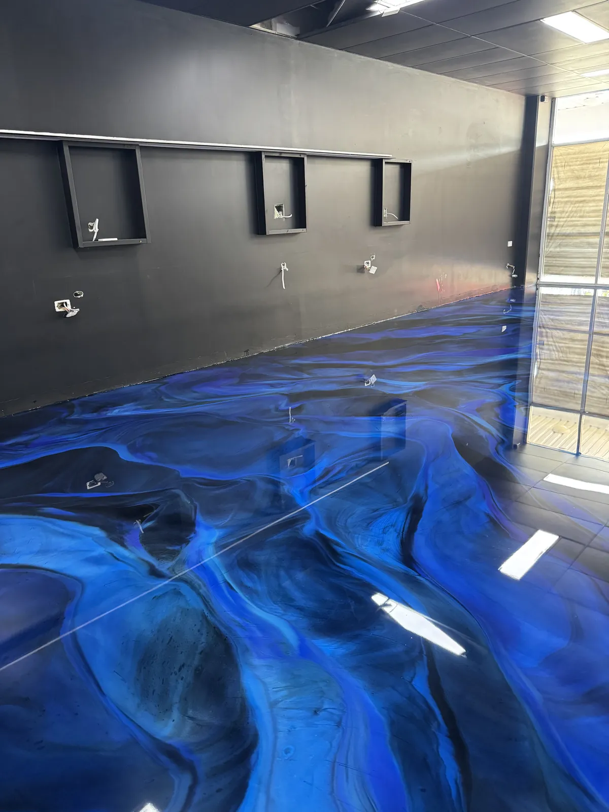 Blue and black metallic epoxy floor with a high-gloss finish in a room with dark feature walls