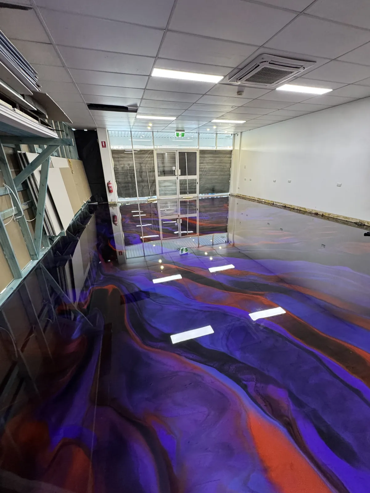 Purple and orange metallic epoxy floor running the length of a commercial tenancy toward the shopfront