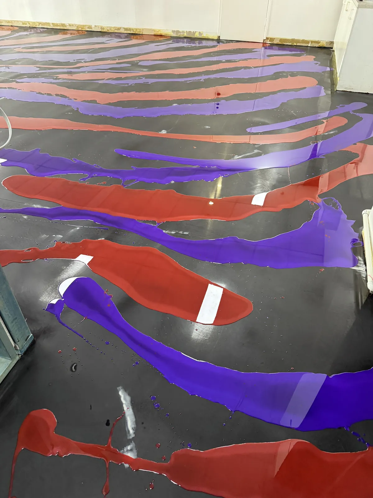 Purple and orange metallic pigment poured in bands across a dark base coat, before it is worked through by hand